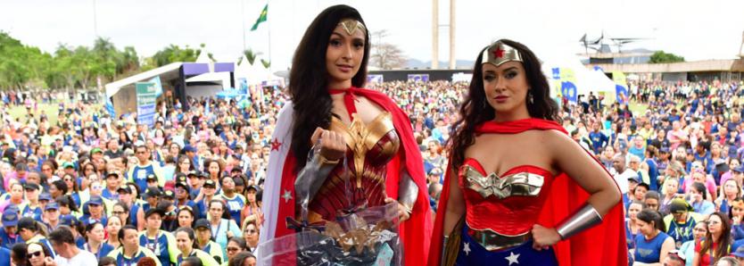 Duas participantes da corrida feminina vestidas de Mulher-Maravilha em frente a uma multidão no Aterro do Flamengo