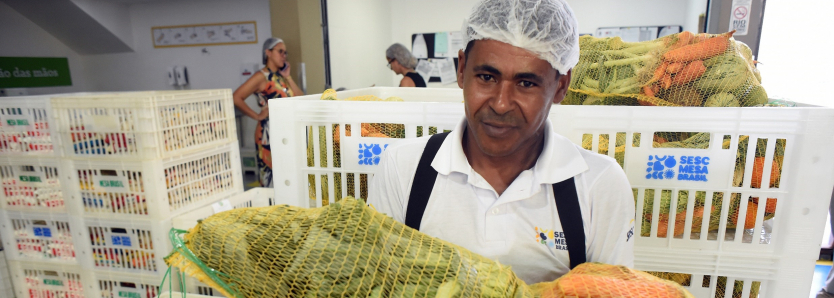 Colaborador do Sesc Mesa Brasil RJ segura uma cesta de alimentos destinados à doação, reforçando o compromisso do programa no combate ao desperdício.
